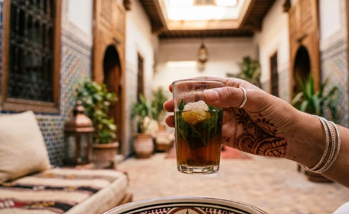 A hand with henna tattoos holding a traditional glass of Moroccan mint tea, a perfect complement to street food in Essaouira.