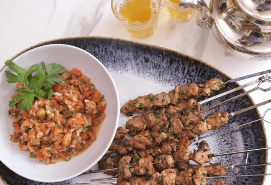 Moroccan street food grilled meat brochettes served on metal skewers with a fresh tomato onion salad and mint tea.