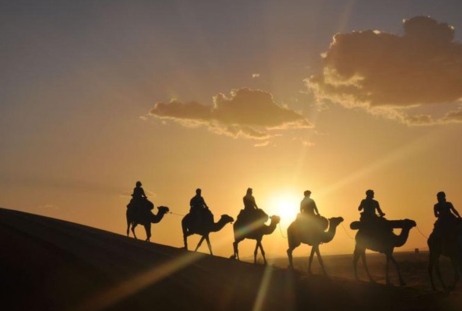 A group of tourists enjoying a golden sunset camel ride in the rocky Agafay Desert near Marrakech.