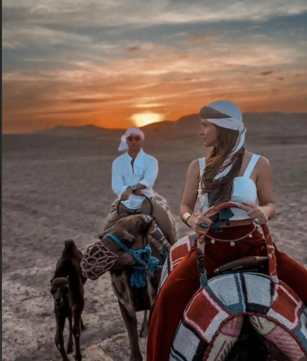 Two travelers wearing traditional headscarves during an affordable camel ride excursion in Morocco.