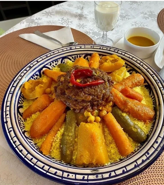 Un plat traditionnel de couscous marocain Tfaya aux sept légumes avec oignons caramélisés et raisins secs, servi avec un verre de Lben.