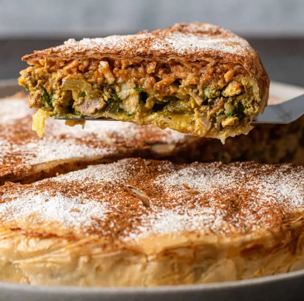 Une part de pastilla croustillante illustrant la gastronomie marocaine avec ses couches de poulet effilé, d'épices, d'œufs et d'amandes concassées, saupoudrée de sucre glace et de lignes de cannelle.