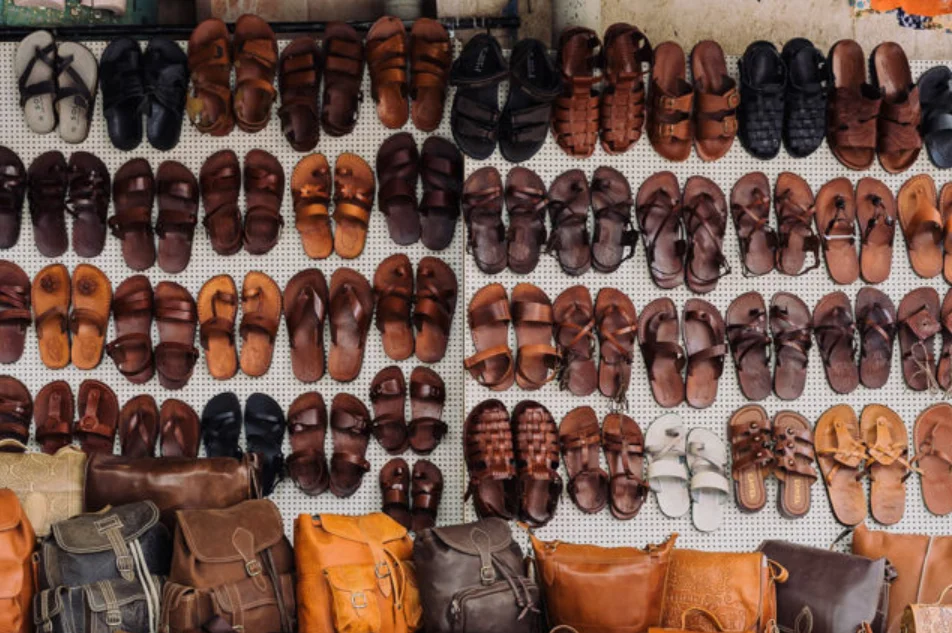 Un étalage de maroquinerie marocaine présentant des rangées de sandales en cuir et des piles de babouches artisanales colorées et brodées.