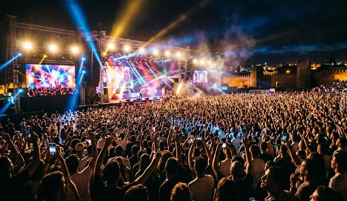 Une foule immense de festivaliers devant la scène géante illuminée de Mawazine 2026 à Rabat à la nuit tombée.