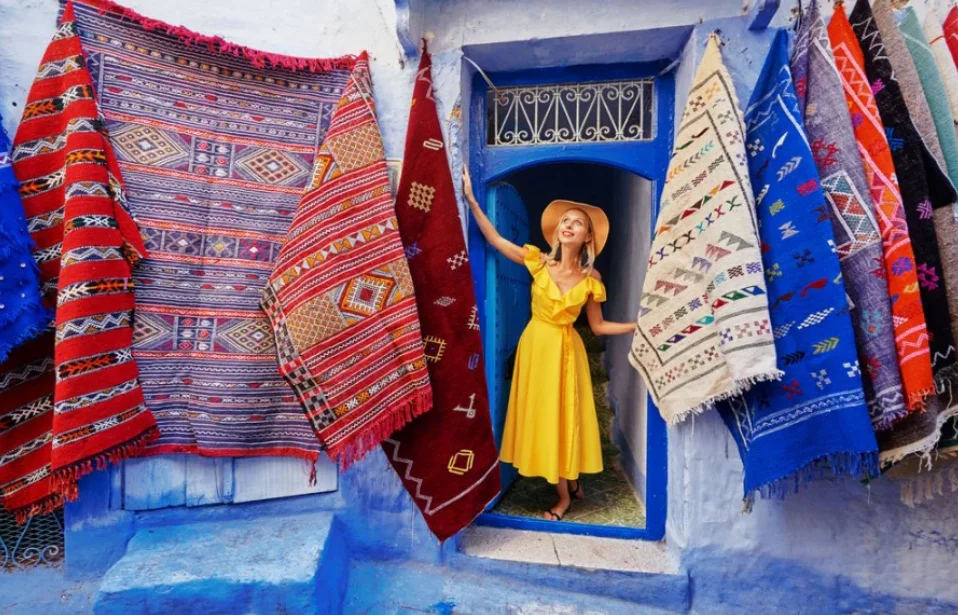 Handmade Moroccan rugs with geometric Berber patterns displayed outside a blue doorway in Chefchaouen.