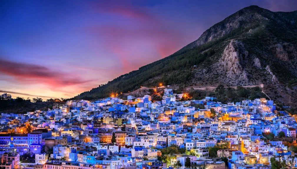 Vue panoramique nocturne de la ville bleue de Chefchaouen éclairée au coucher du soleil, un incontournable pour voyager au Maroc.