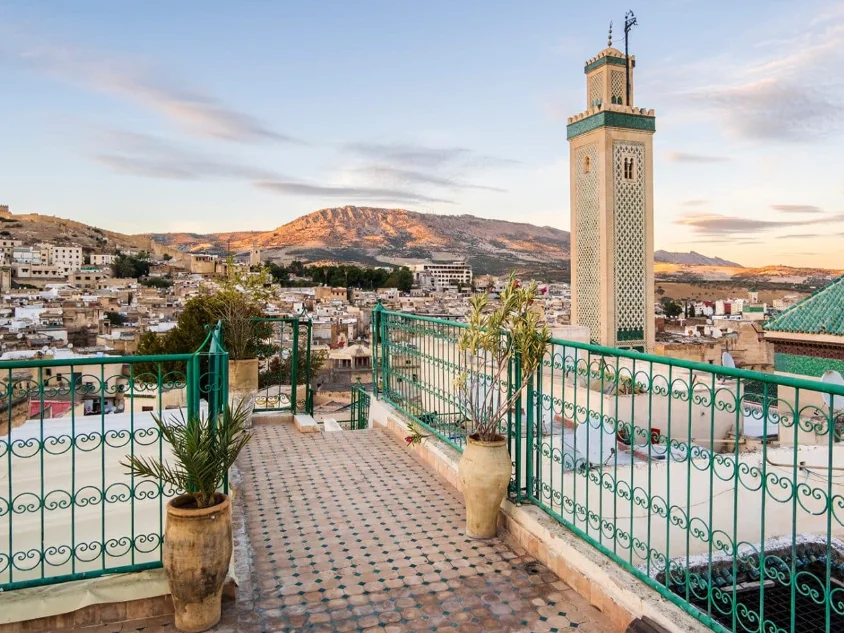 Vue depuis un riad sur la médina de Fès et un minaret traditionnel au lever du soleil, idéal pour illustrer un guide pour voyager au Maroc.