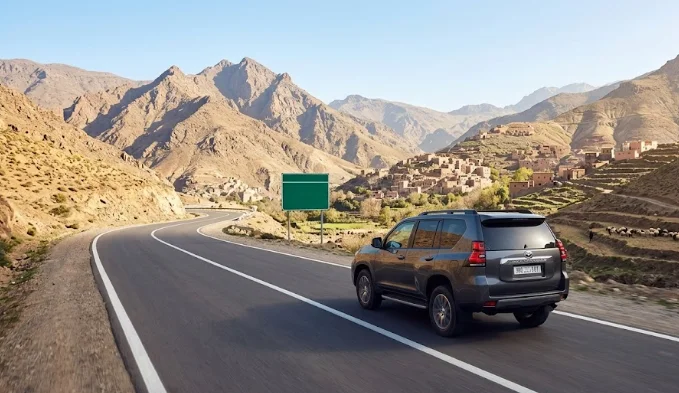 Vue panoramique d'un SUV 4x4 gris foncé en train de conduire au Maroc sur une route de montagne sinueuse dans l'Atlas, se dirigeant vers un village berbère.