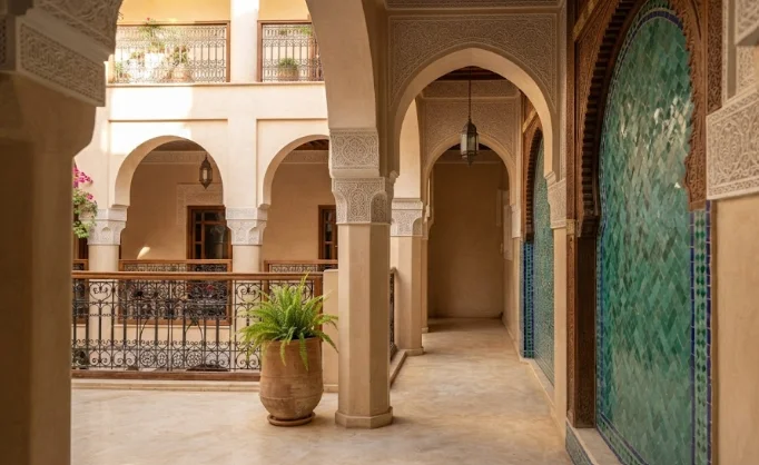 Une vue architecturale détaillée d'un couloir de riad marocain, mettant en valeur le travail de stuc ciselé, les garde-corps en fer forgé et la texture unique des carreaux de zellige vert émeraude.